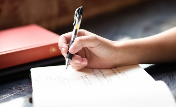 Image of a woman's hand writing in a notebook tips to become a better writer